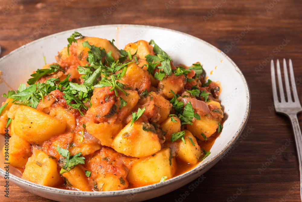 Greek vegetable stew of potatoes and vegetables in tomato sauce in a plate on a wooden table, top view, close-up Greek vegetable stew of potatoes and vegetables in tomato sauce in a plate on a wooden table, top view, close-up