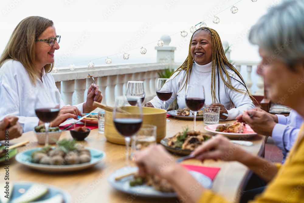 Happy multiracial senior friends having fun dining together on house patio - Elderly lifestyle people and food concept