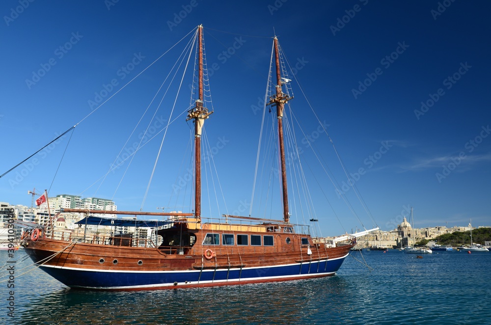 Cruise sailboat in the port of Tas Sliema, Valletta, Malta. A wooden sailboat waits in the harbor on a sunny day on the calm sea.