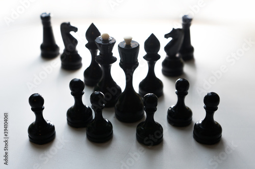 Wooden chess pieces. Black king Queen surrounded by her large retinue, full set of black side chess game, counter light, all pieces in shadow