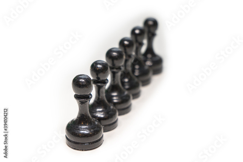 Wooden chess pieces. Black pawns stand behind each other looking out from behind their comrades on a white background