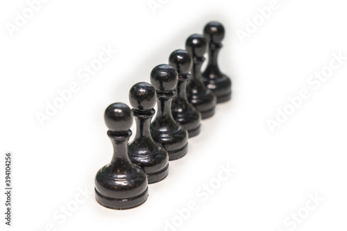 Wooden chess pieces. Black pawns stand behind each other looking out from behind their comrades on a white background