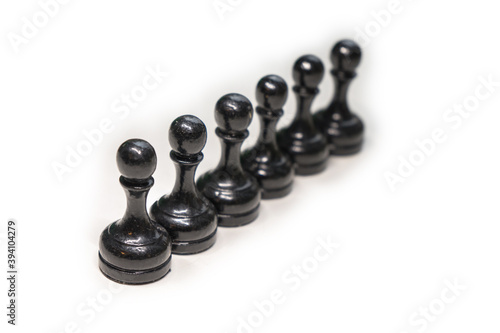Wooden chess pieces. Black pawns stand behind each other looking out from behind their comrades on a white background