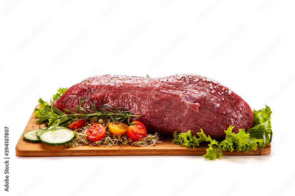 Fresh raw beef on cutting board with fresh vegetables on white background
Fresh raw beef on cutting board with fresh vegetables on white background