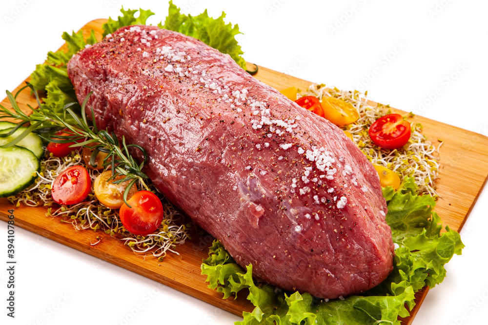 Fresh raw beef on cutting board with fresh vegetables on white background
Fresh raw beef on cutting board with fresh vegetables on white background