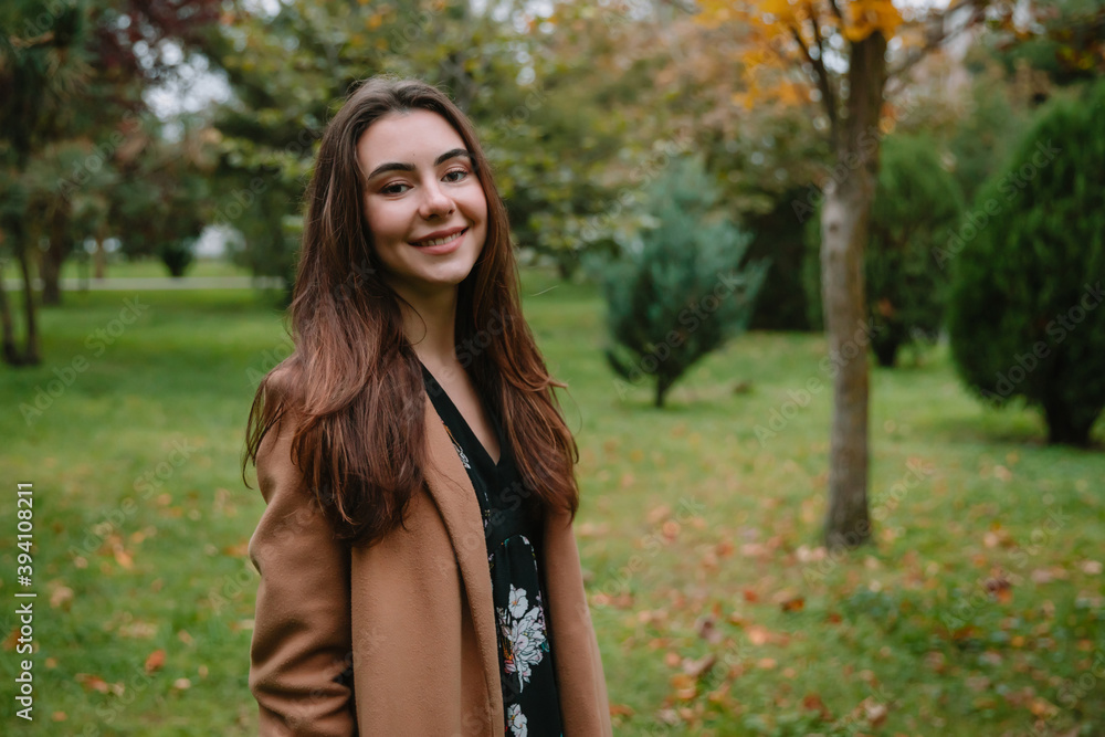 Portrait of young attractive woman in park. Woman in beige coat Portrait of young attractive woman in park. Woman in beige coat