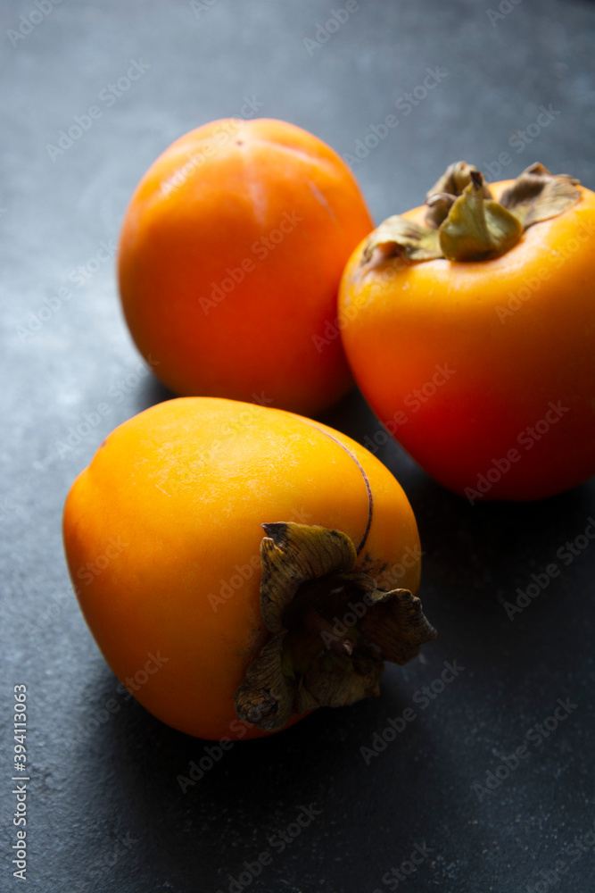 Whole sweet orange persimmon fruits isolated on dark background. Copy space. Whole sweet orange persimmon fruits isolated on dark background. Copy space.