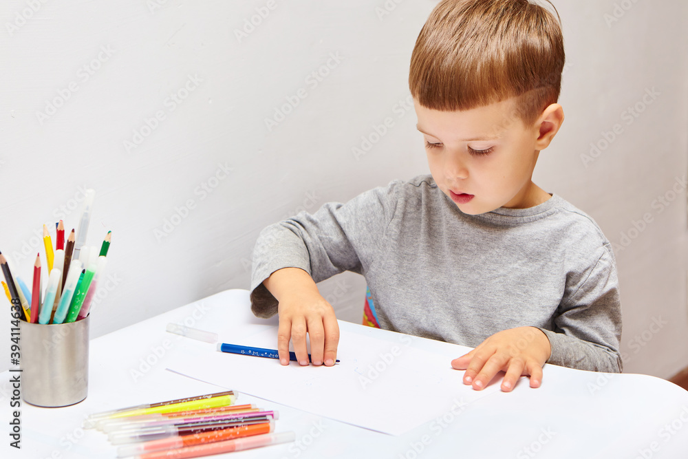 Cute little boy with blond hair draws colored pencils at home. Draws at the white table. Cute little boy with blond hair draws colored pencils at home. Draws at the white table.