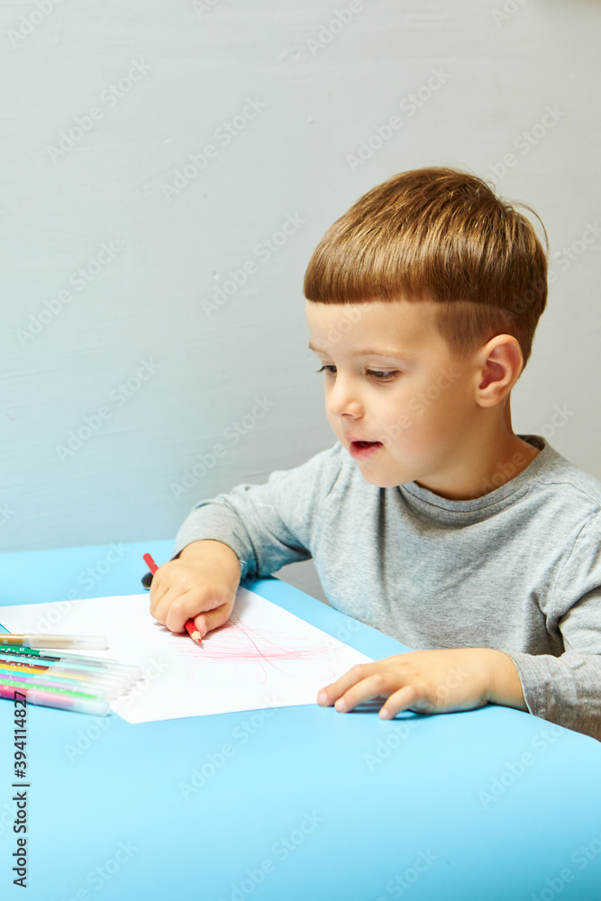 Cute little boy with blond hair draws colored pencils at home. Draws at the blue table. Cute little boy with blond hair draws colored pencils at home. Draws at the blue table.