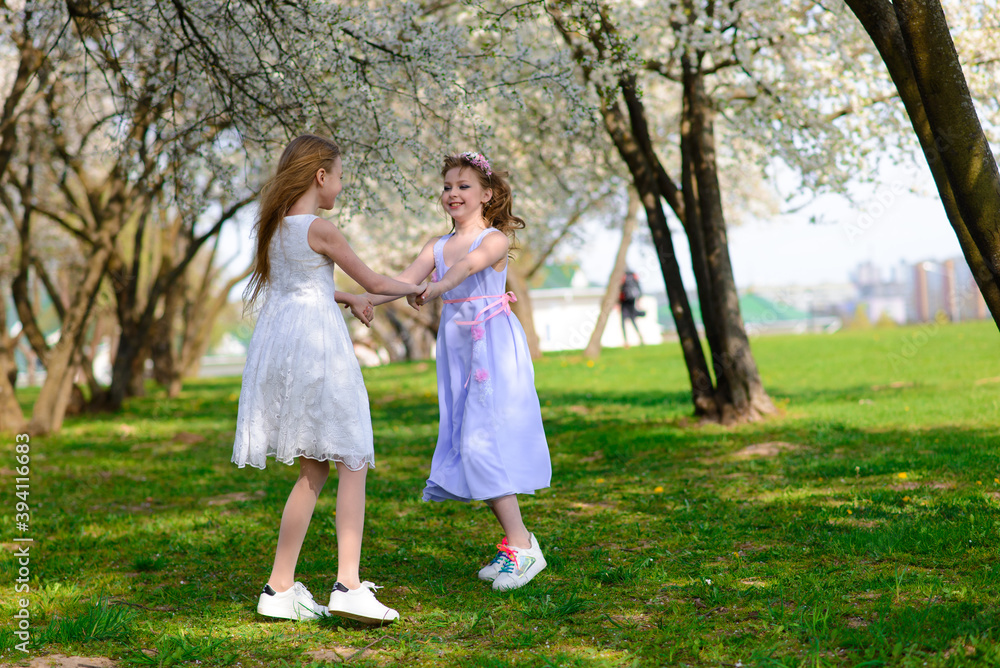 Young girls with blue eyes in white dresses in garden with apple trees blosoming Young girls with blue eyes in white dresses in garden with apple trees blosoming