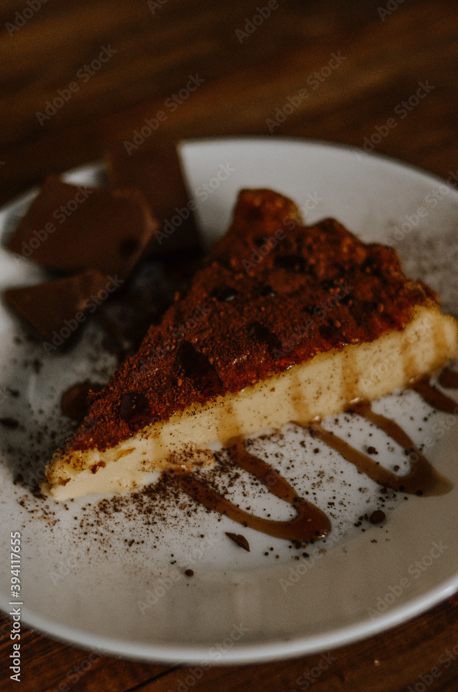 Tasty slice of coffee cheesecake covered with cacao on white plate with chocolate and caramel on dark wooden background close up Tasty slice of coffee cheesecake covered with cacao on white plate with chocolate and caramel on dark wooden background close up