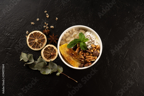 Oatmeal in a round white plate with yogurt, chia seeds, banana and walnut, decorated with mint leaves and chocolate drops. Healthy vegetarian meal.