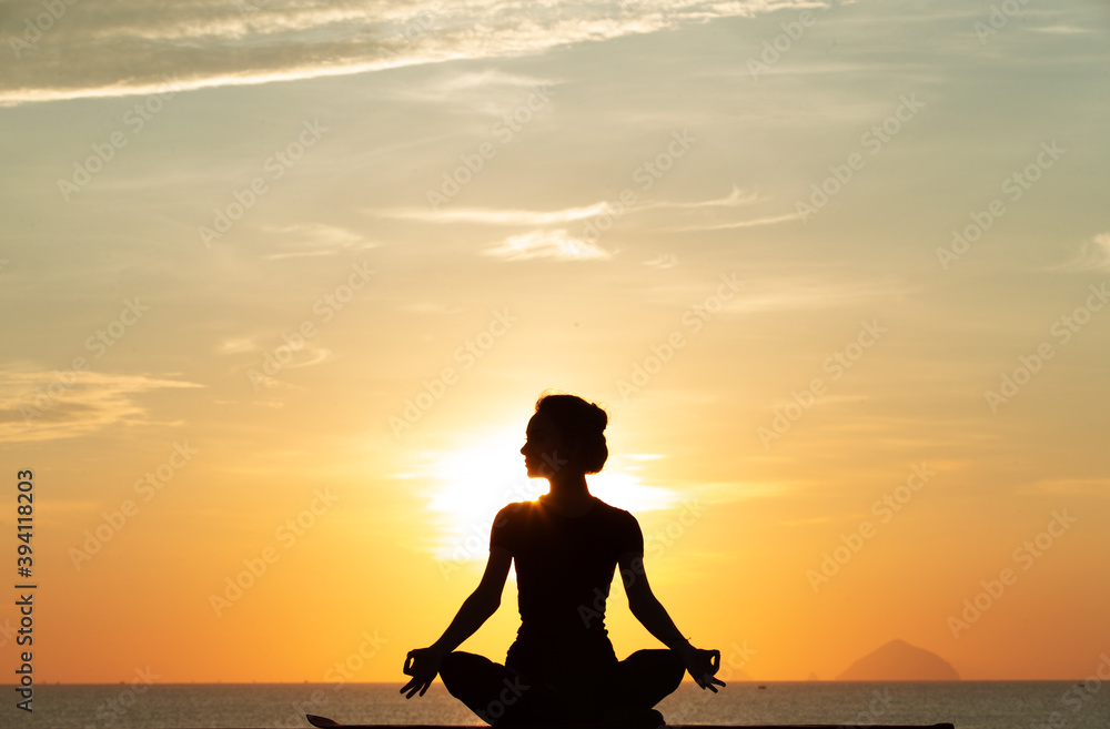 Silhouette of a young woman doing yoga near the sea at sunset.