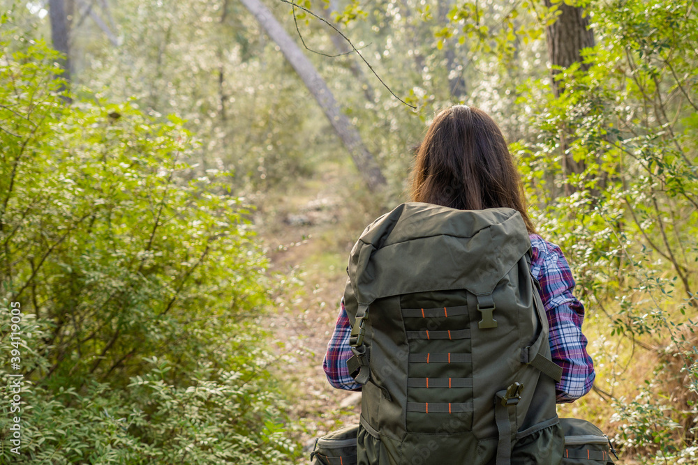 Young woman from behind walking hiking on a mountain path in mediterranean landscape, mallorca, woman wears plaid shirt and jeans