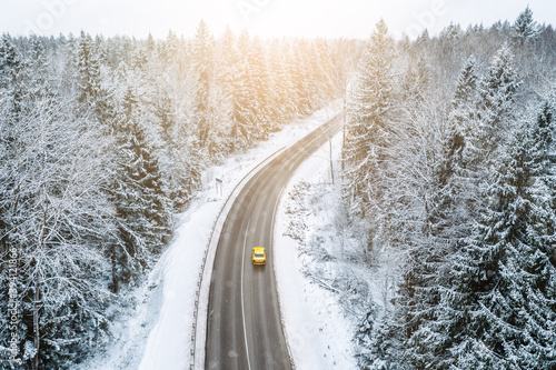 Aerial view of winter road with car and snow covered trees in the forest photo