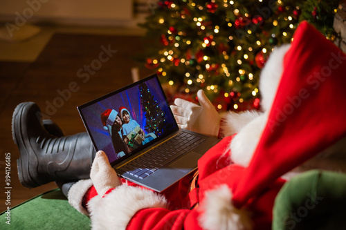 Happy mom and son talking to santa claus by video chat on a laptop. Woman and boy remotely wishes Merry Christmas photo