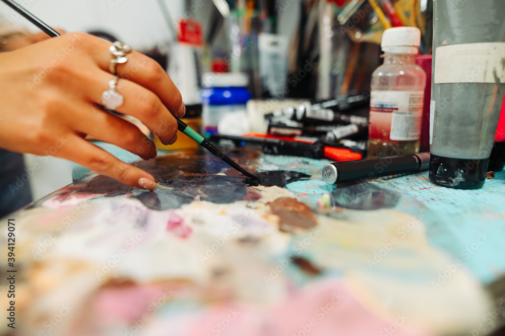 Woman artist mixes paint with a brush on a palette with oil. Close photo of hands with brush. Background
