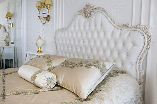 King size bed with cushioned and buttoned headboard in hotel room with classic baroque style interior. Close up, copy space, background. photo