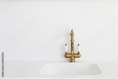 Close up shot of a vintage two handle faucet in a white minimalistic style kitchen. Copper retro styled water mixer. Copy space, background photo