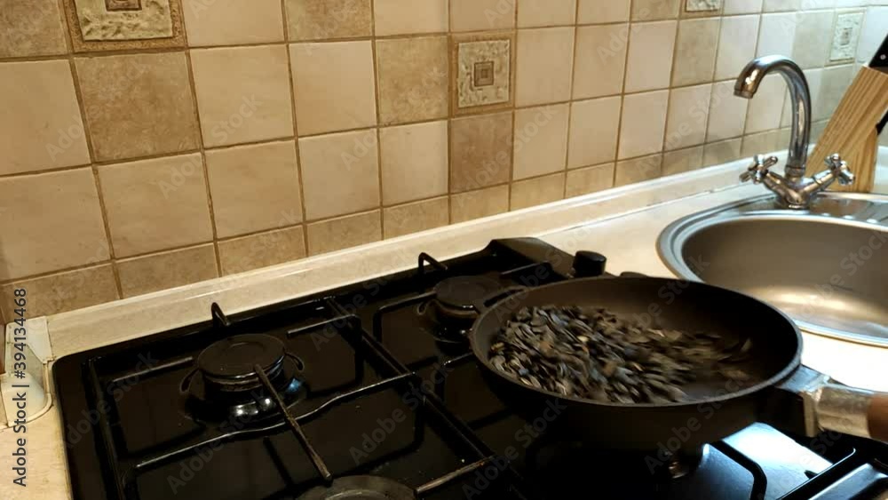 Man fries sunflower seeds on the pan stirring them. Closeup sunflower