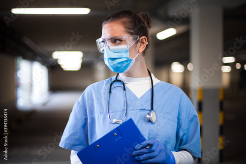 Female ICU doctor in hospital parking lot,first responder frontline key medical worker,holding clipboard patient medical card,looking away,emergency service during COVID-19 coronavirus pandemic crisis photo