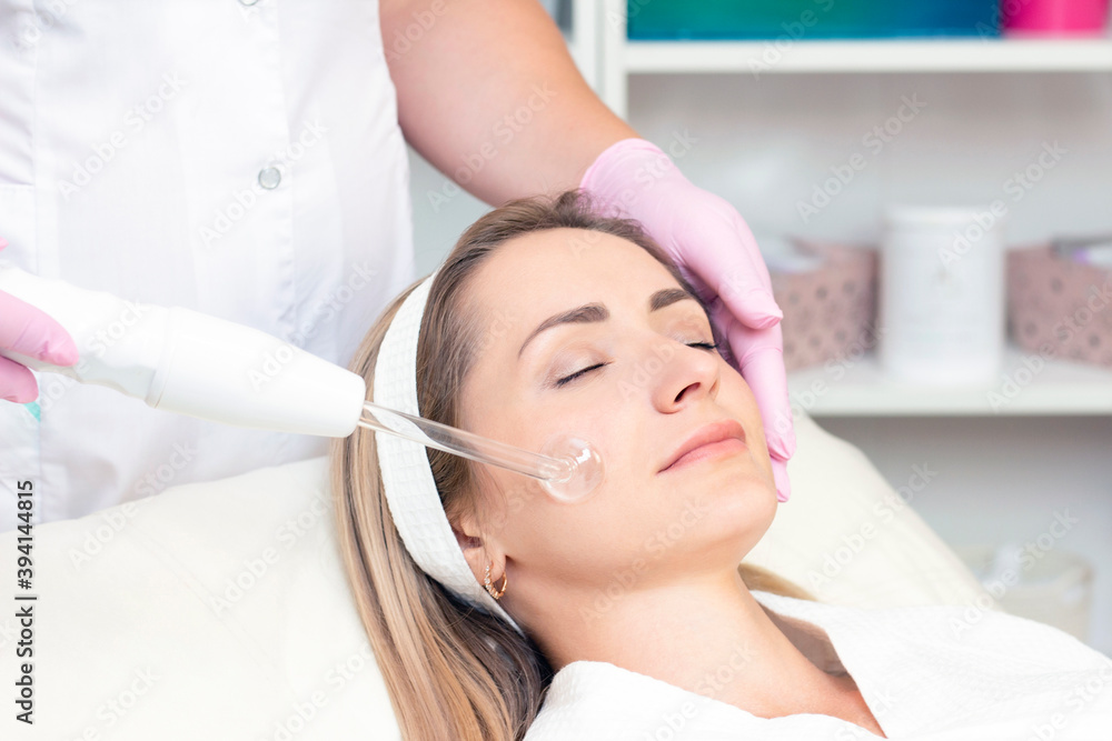 Cosmetologist performs a pulse current procedure for the face of a young woman. Cosmetologist performs a pulse current procedure for the face of a young woman.