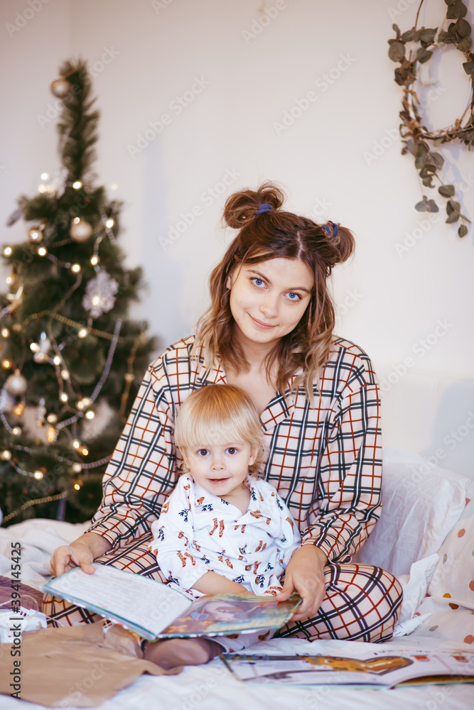 Portrait of a happy mother and a charming child at Christmas in a bright interior reading a book together Portrait of a happy mother and a charming child at Christmas in a bright interior reading a book together