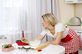 A joyful woman in the kitchen cook Christmas cake and  talking on his cell phone smartphone. Woman preparing Christmas holiday cookies. Christmas baking. Cooking homemade cake at home 