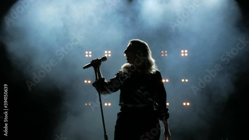 Silhouette of a girl comes to the microphone on the stage against a background of bright yellow lights