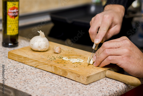 Man cutting garlic with a knife on a wooden board