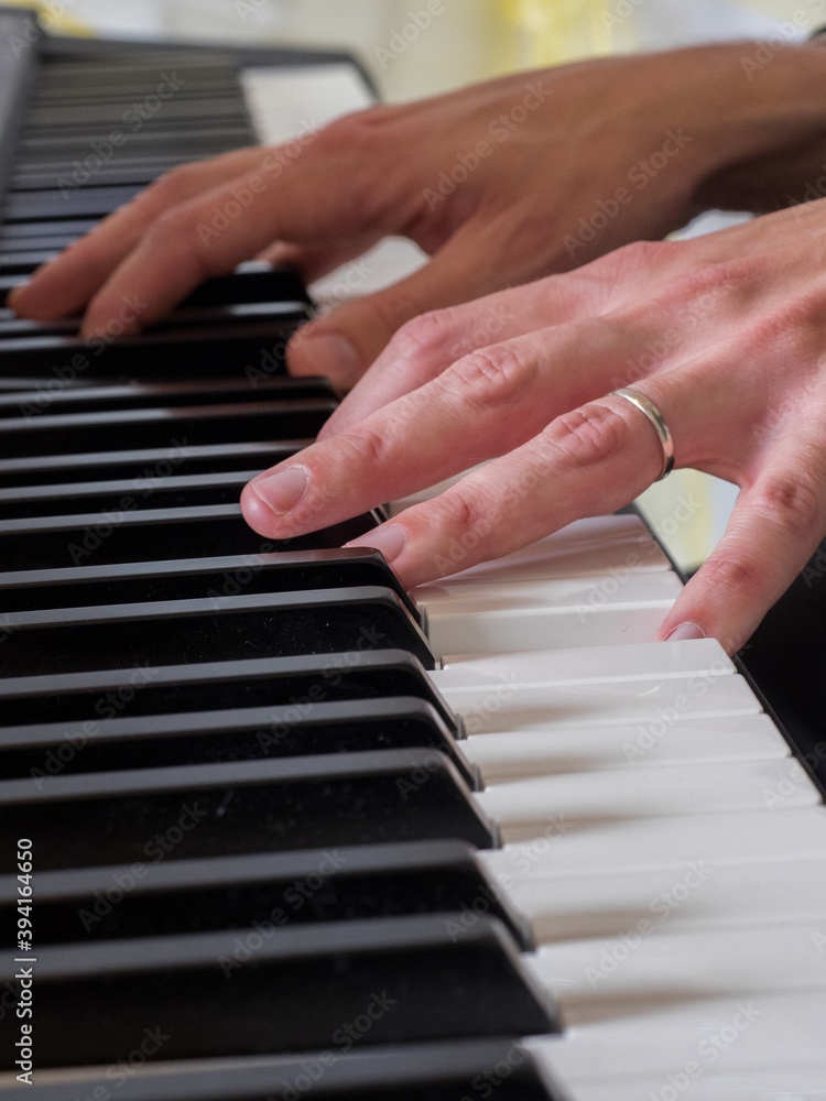 Fototapeta premium Close up point of focus on one of two hands playing a keyboard.Wedding ring on finger.Musician.Vertical Image