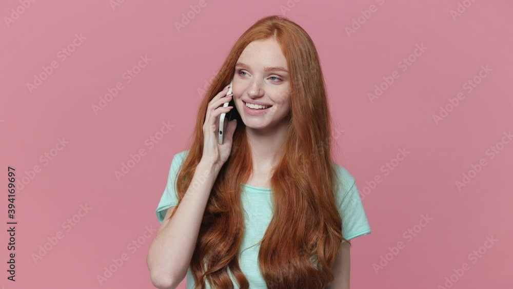 Smiling shocked redhead young woman in casual blue turquoise t-shirt posing isolated on pink background studio. People lifestyle concept. Talking on mobile phone say wow doing winner gesture blinking Smiling shocked redhead young woman in casual blue turquoise t-shirt posing isolated on pink background studio. People lifestyle concept. Talking on mobile phone say wow doing winner gesture blinking