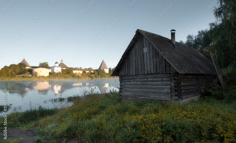 log wooden house on background Fortress in the city of Staraya Ladoga on the Volkhov River with a foggy psummer dawn, Old Architecture in the landscape of the Russian North