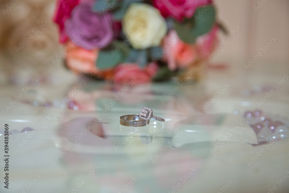 Glass table . Wedding rings next to a red flower bouquet selective focuse . Bride and groom with Engagement gold rings put on the table, and next to them lies a wedding bouquet . Glass table . Wedding rings next to a red flower bouquet selective focuse . Bride and groom with Engagement gold rings put on the table, and next to them lies a wedding bouquet .