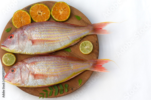 Close up view of fresh Pink Perch (thread finned Bream) Decorated with lemon slice,Orange slice and curry leaves on a wooden pad,White Background,Selective focus. photo