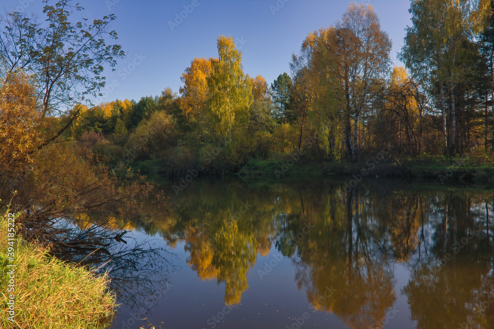 Autumn landscape, forest trees are reflected in calm river water against a background of blue sky and white clouds. Autumn landscape, forest trees are reflected in calm river water against a background of blue sky and white clouds.