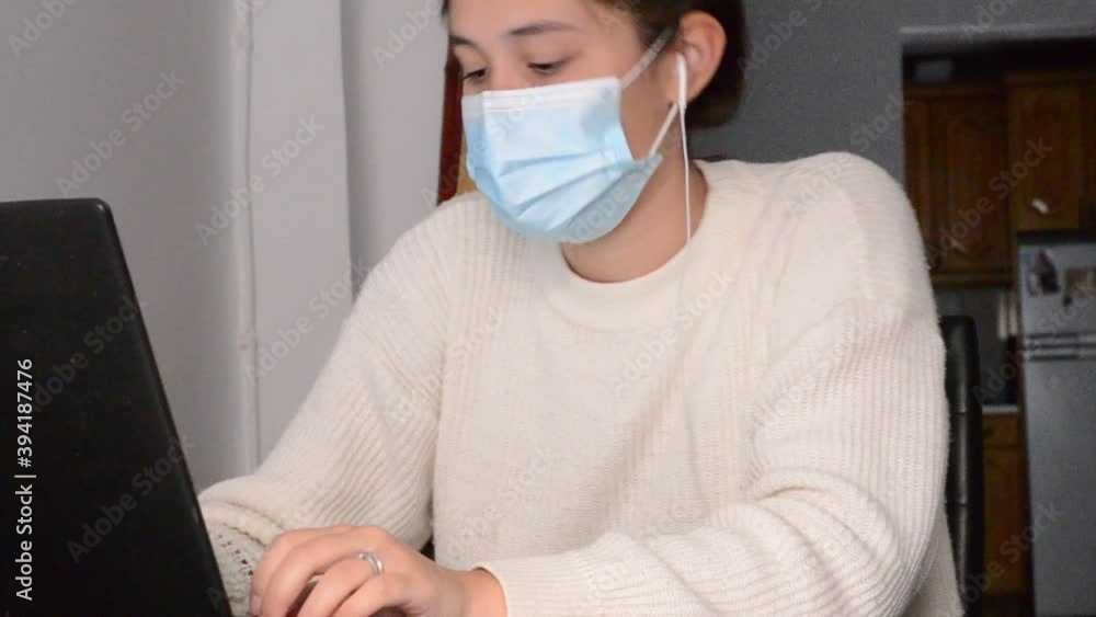 mujer de pelo negro con mascarilla sanitaria trabajando en casa con ordenador portátil