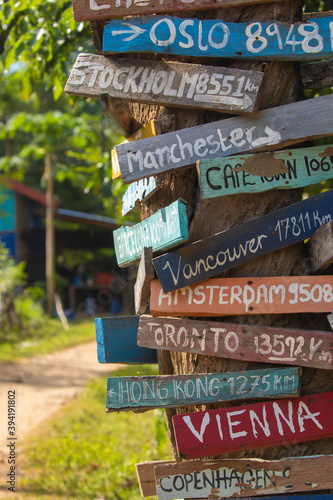 Colourful hand painted direction wood signs to different cities of the world, and mileage marker in Don Det island, one of the famous Four Thousand Islands or Si Phan Don, in the Mekong river, Laos.