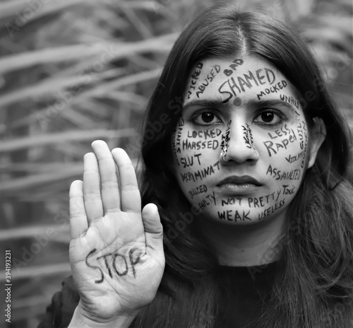 Black and white photo of a southeast Asian brown woman anti gender based violence messages written all of her face protesting against violence against women and girls and saying to stop violence  photo