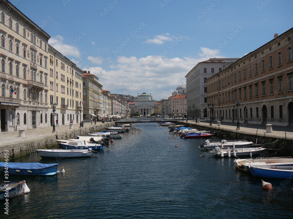 Panorama of Borgo Teresiano in Trieste, characterized by the Grand Canal, ancient buildings on both sides, and by the Church of San Paolo with neoclassical style positioned in front.