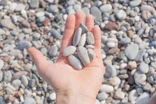 A woman's hand with gray sea stones on the palm close-up against the background of a pebble beach