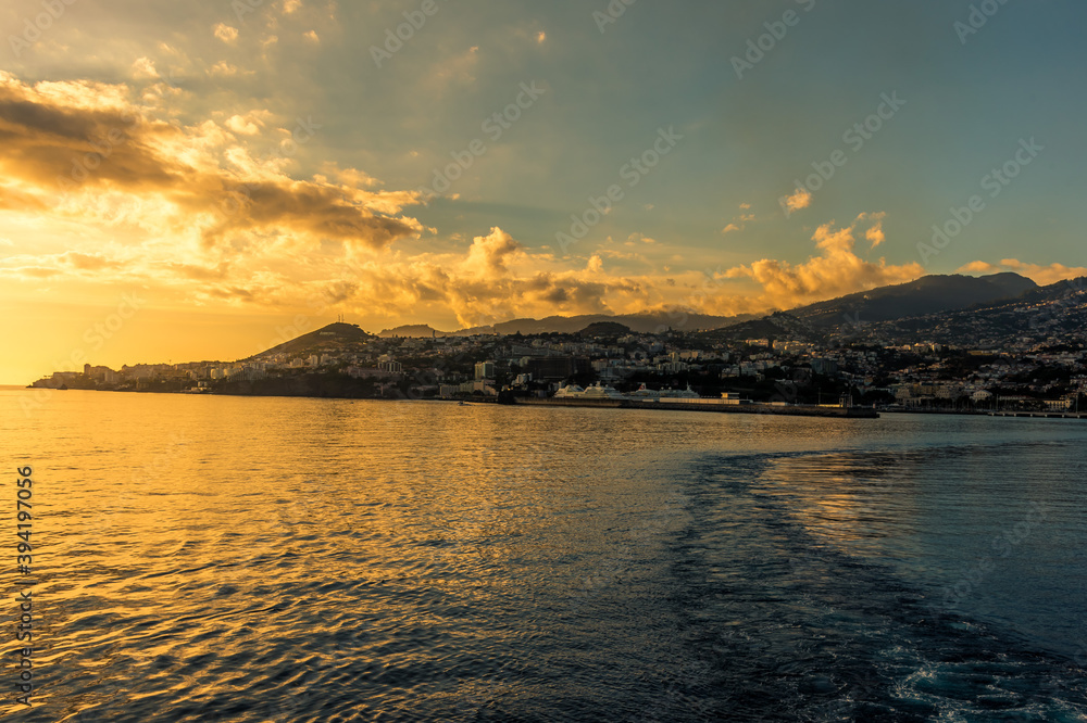 A golden sunset over the city of Funchal, Madeira viewed from a ship sailing away from the island
