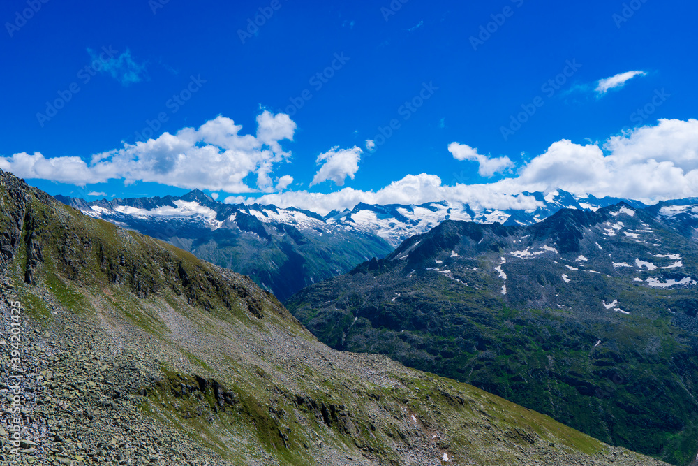 Landscape mountain view peaks in snow and green hills, deep blue sky and huge white clouds background, Hohe Tauern Austrian Alps, Europe