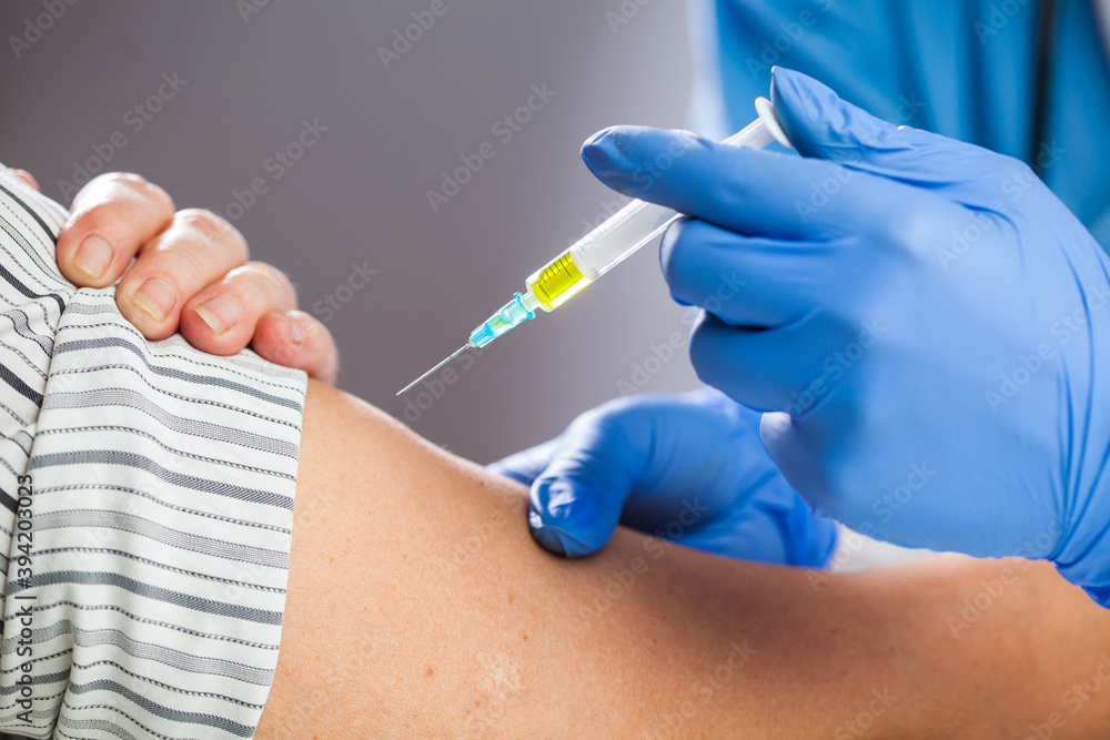 Coronavirus COVID-19 immunisation concept,medical worker wearing blue protective latex gloves holding syringe filled with yellow liquid,giving patient vaccine shot dose,caucasian hand closeup detail Coronavirus COVID-19 immunisation concept,medical worker wearing blue protective latex gloves holding syringe filled with yellow liquid,giving patient vaccine shot dose,caucasian hand closeup detail