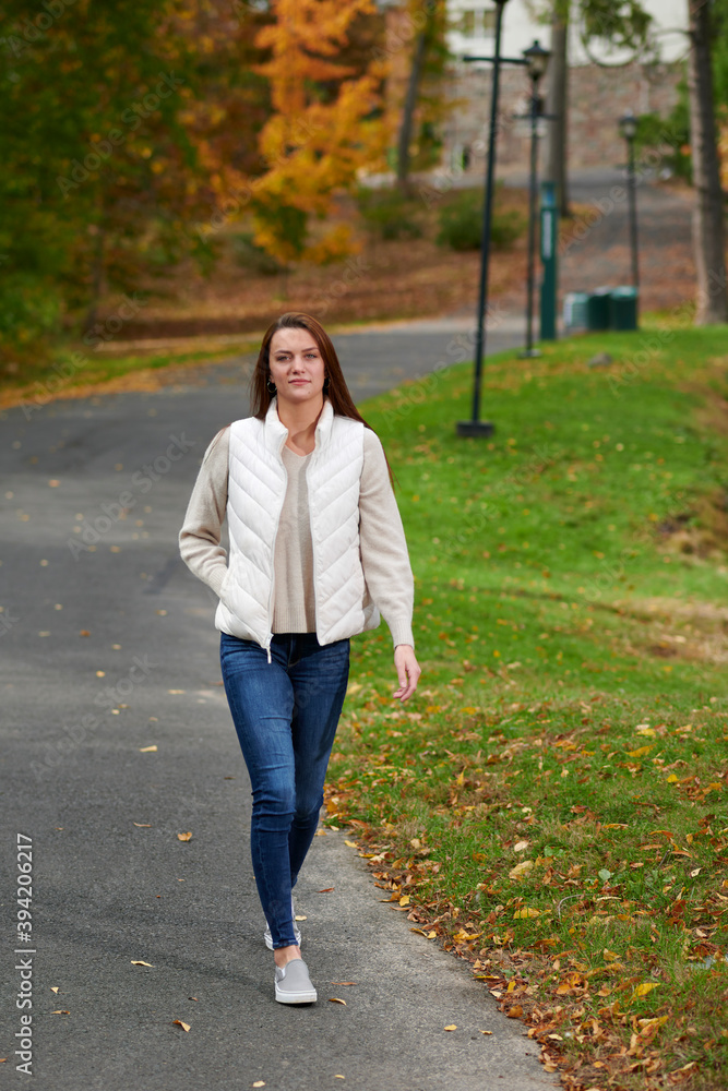 Stunning young woman on college campus in fall wearing blue jeans and white down vest Stunning young woman on college campus in fall wearing blue jeans and white down vest