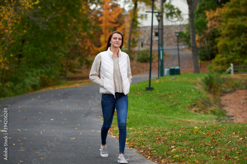 Stunning young woman on college campus in fall wearing blue jeans and white down vest photo