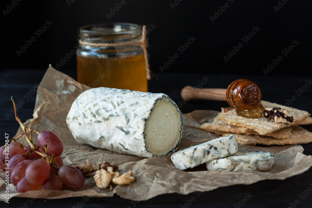 Fototapeta premium Delicious goat chevre cheese slices with grapes, honey and nuts on a dark wooden background.