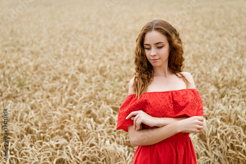 Beautiful young woman in red dress in a wheat field © Екатерина Переславце