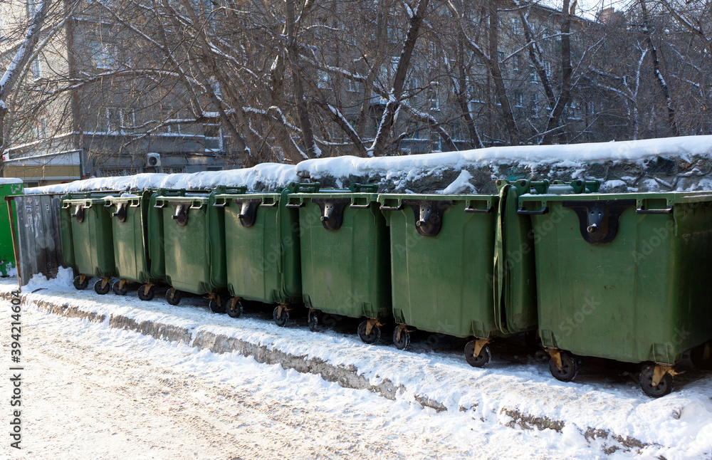 Контейнеры для мусора зеленого цвета на колесах засыпаны снегом