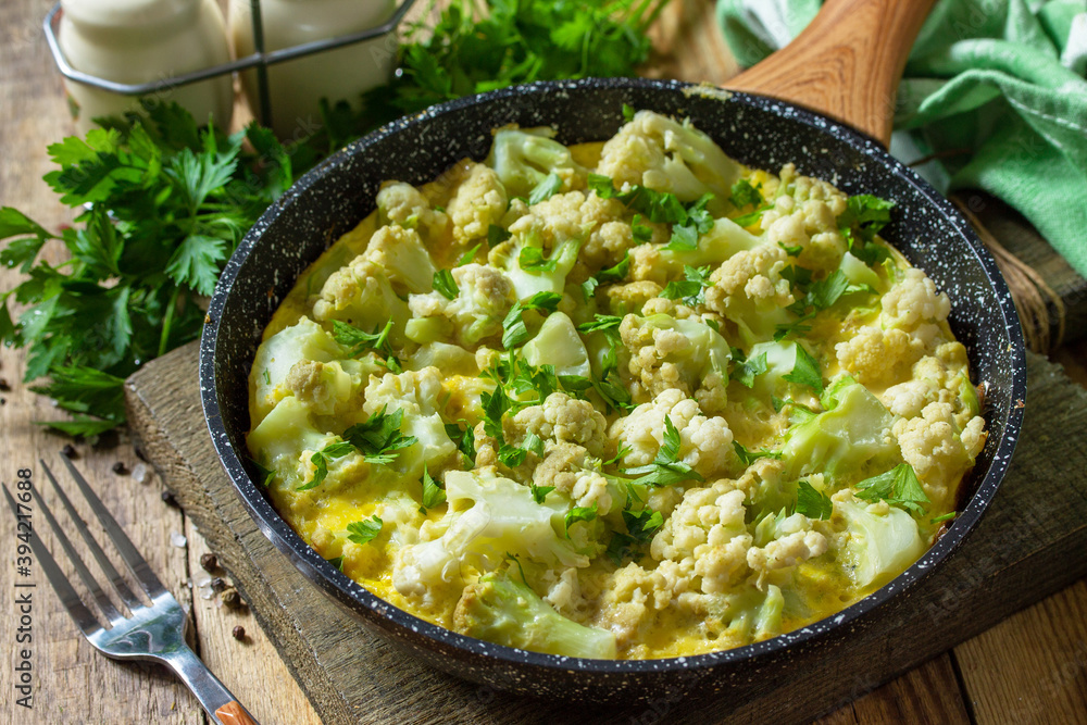 Diet breakfast or healthy lunch. Egg omelet with cauliflower in a cast-iron pan on rustic wooden table. Diet breakfast or healthy lunch. Egg omelet with cauliflower in a cast-iron pan on rustic wooden table.